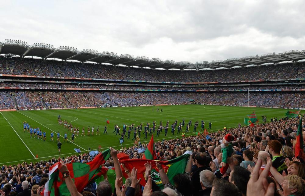 Crowded stadium with teams lining up on the field, fans waving flags in the stands.