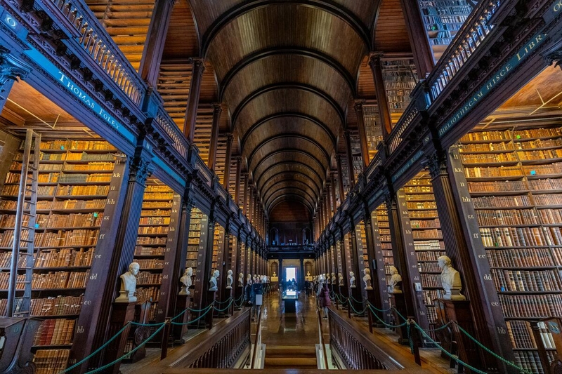 Ornate library with high wooden arches, shelves full of books, and marble busts lining the walkway.