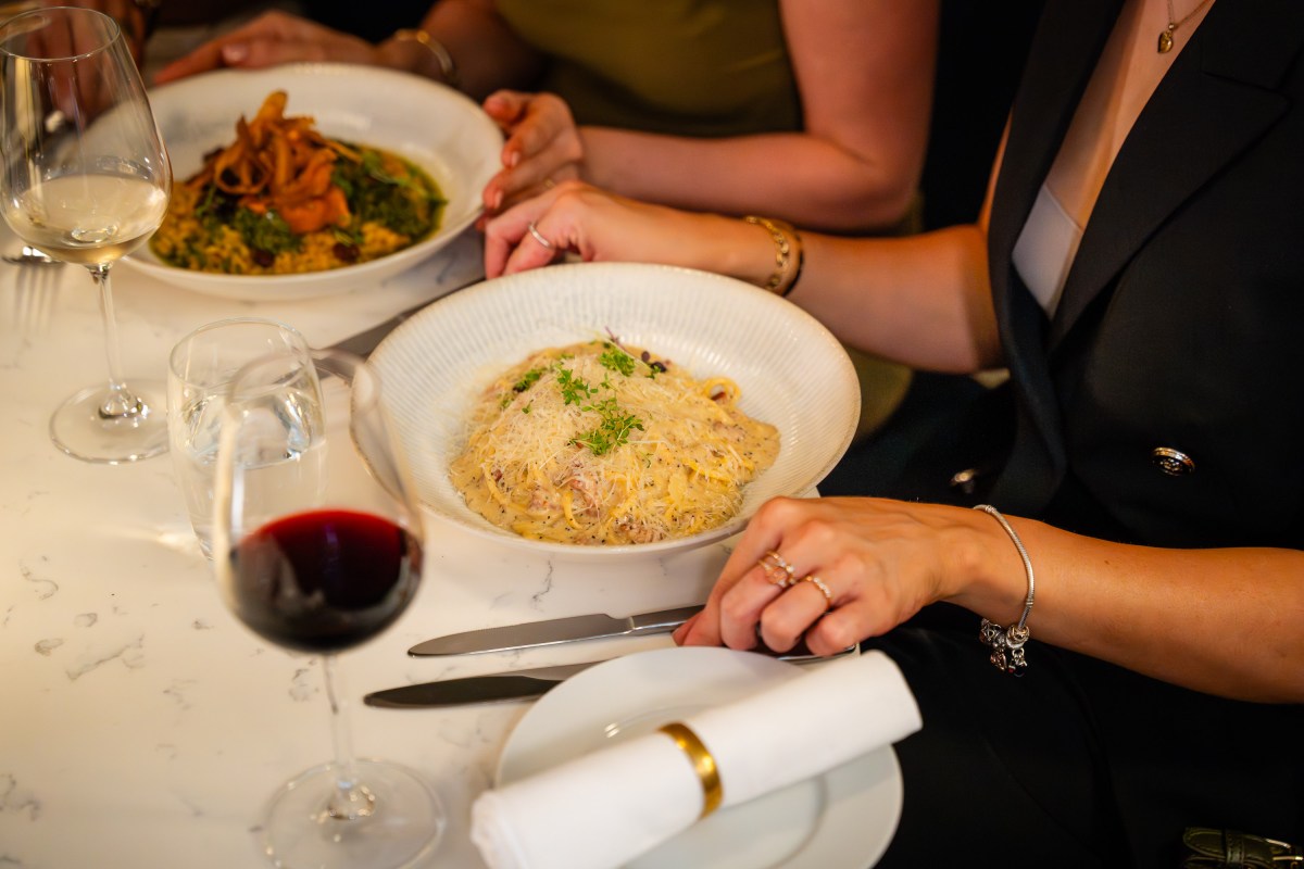 Two people dining with pasta dishes and wine on a white table.