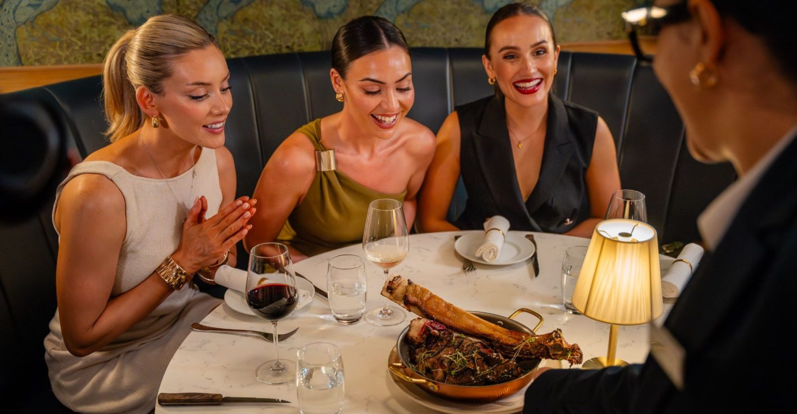 Three women at a restaurant table enjoy a dish being served by a waiter.